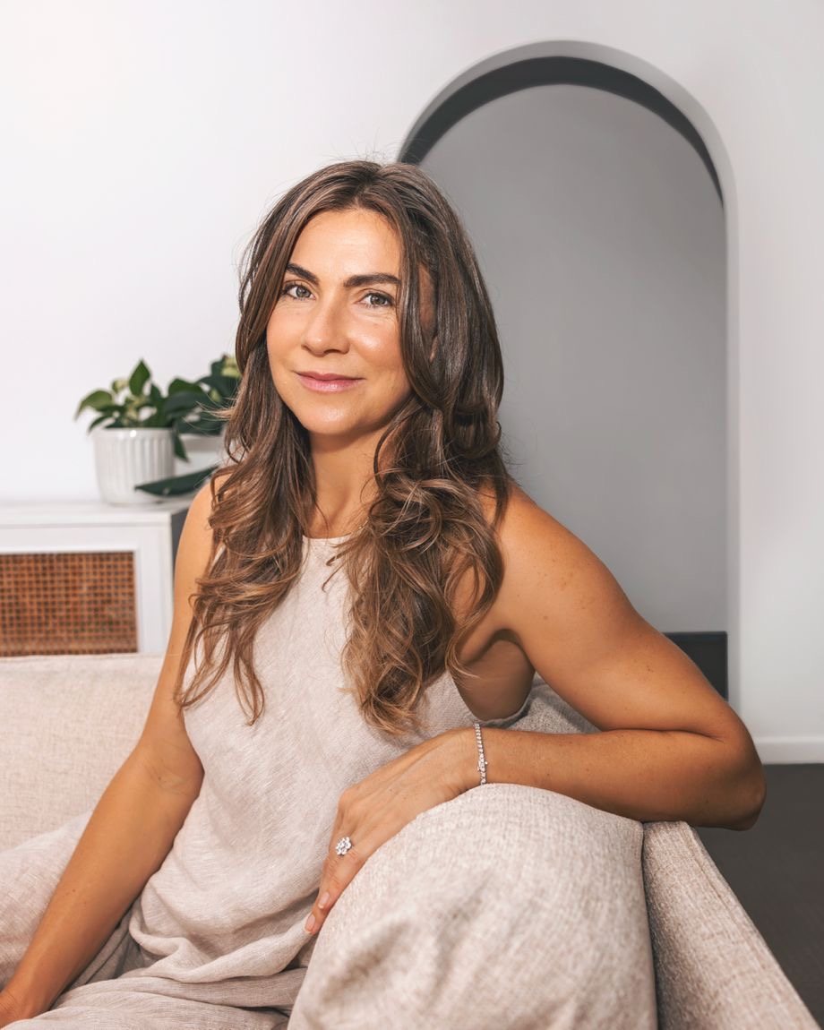 Cortney Thomson seated on a linen armchair in a bright room, smiling at the camera