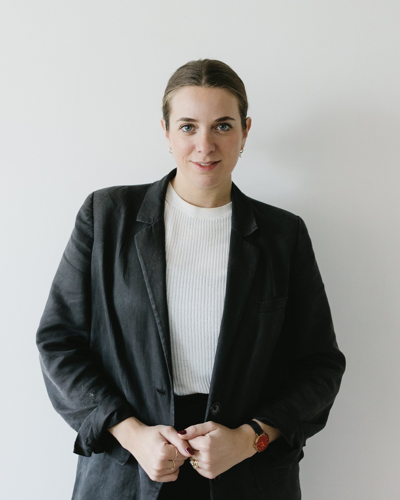 Jami Emerson Cheneval standing against a pale wall in a dark blazer and white top